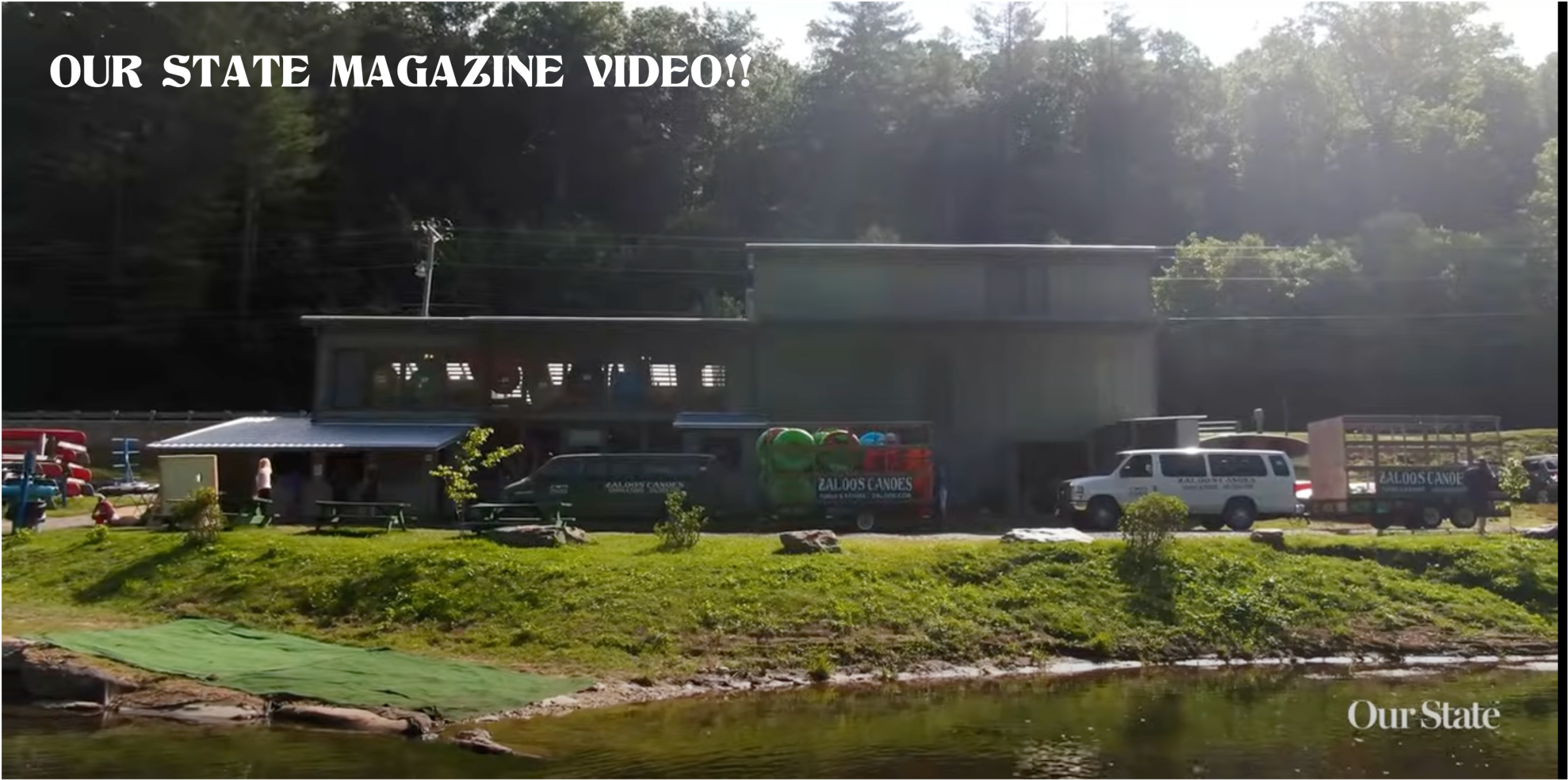 Outdoor building by water with canoes and text 'OUR STATE MAGAZINE VIDEO!!'