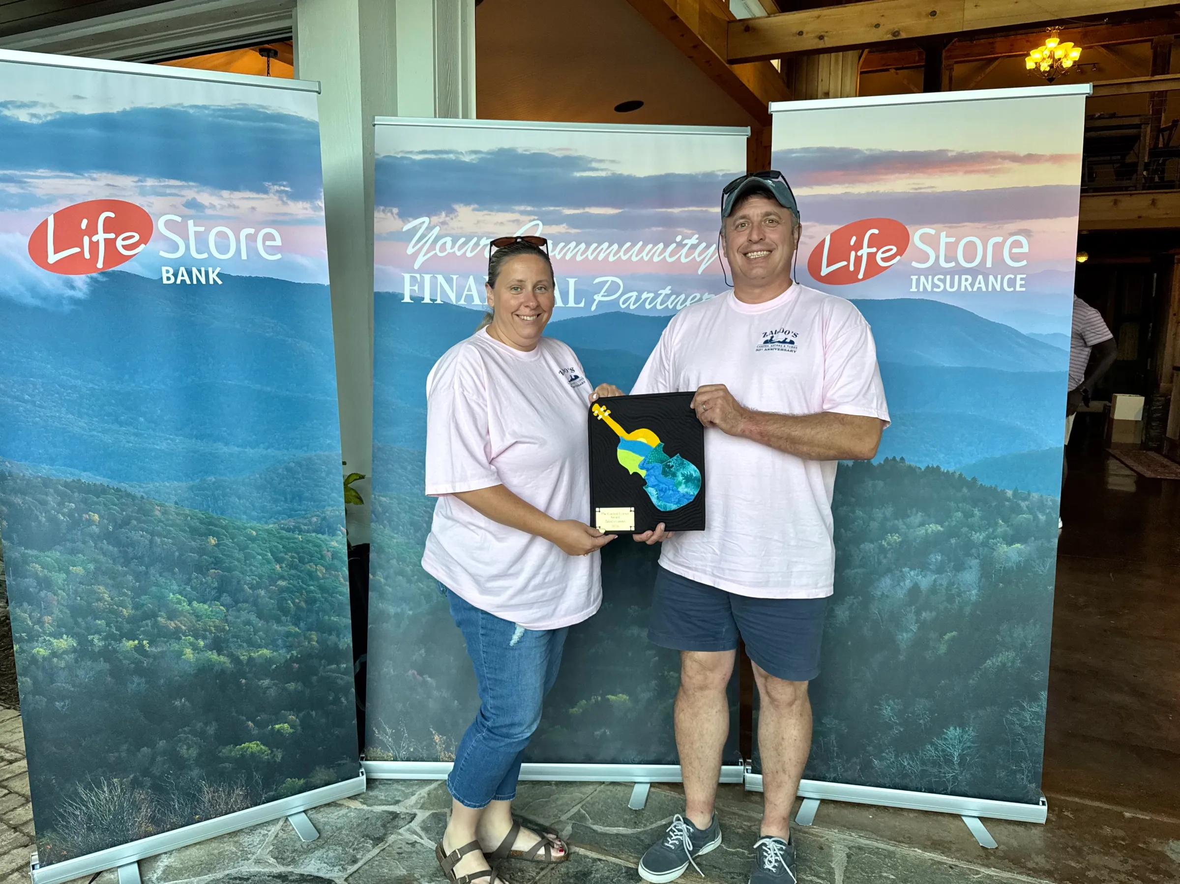 Two people holding a plaque, standing between banners for LifeStore Bank and Insurance.